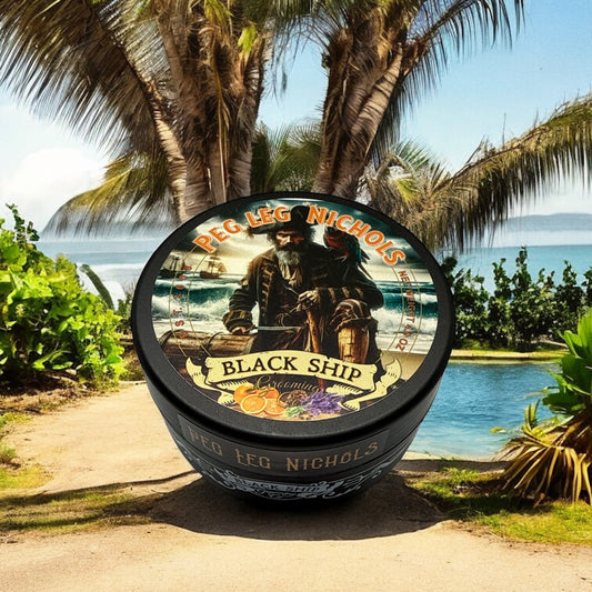 Jar of Peg Leg Nichols Black Ship Shaving soap on a beach with palm trees and ocean in the background